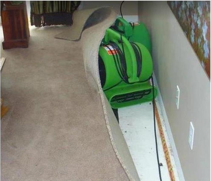 water damaged room. carpeting pulled back from wall as SERVPRO drying equipment dries floor and drywall